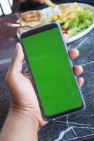 mano de hombre joven usando un teléfono inteligente con pantalla verde en el café foto