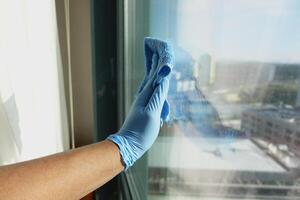 hand in blue glove cleaning window with green rag photo