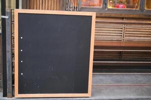 Empty wooden blackboard mockup standing outdoors in front of cafe photo