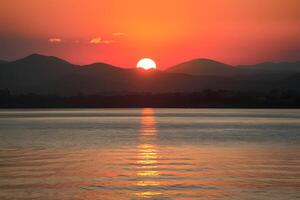 AI generated Mountains provide stunning backdrop to serene sunset over water photo