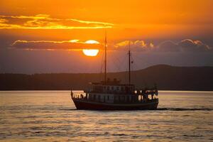 ai generado barco se desliza debajo puestas de sol dorado resplandor en lago baikal foto