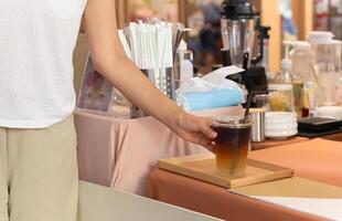 mujer tomando con hielo café en un tomar lejos taza desde café encimera. foto