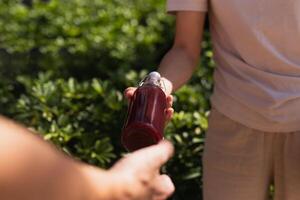 Woman's hand giving a glass bottle of nutritious juice drink with plant leaf background. photo