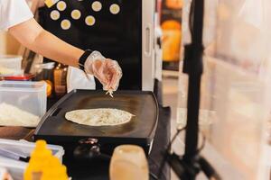 Chef sprinkles a tortilla with cheese preparing fresh quesadilla on black grill. photo