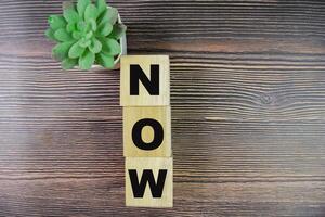 Concept of The wooden Cubes with the word NOW on wooden background. photo