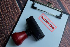 Red Handle Rubber Stamper and Patented text above paperwork isolated on wooden background photo