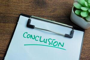 Concept of conclusion write on paperwork isolated on wooden background. photo
