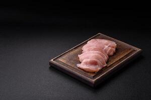 Slices of raw chicken or turkey fillet with salt, spices and herbs photo