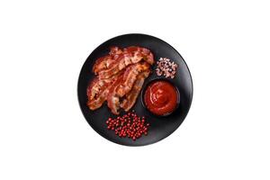 Delicious fresh fried bacon with salt and spices on a dark background photo