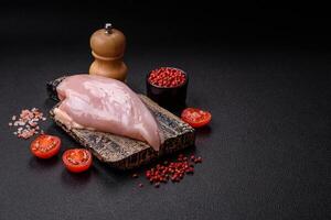 Filete de pollo fresco sobre una mesa de hormigón oscuro con especias y hierbas. foto