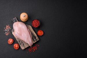 Filete de pollo fresco sobre una mesa de hormigón oscuro con especias y hierbas. foto