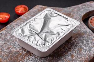 Rectangular plastic box with yogurt or cheese hermetically sealed with a foil lid photo