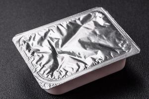 Rectangular plastic box with yogurt or cheese hermetically sealed with a foil lid photo