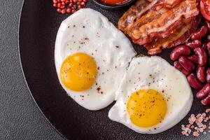 English breakfast with fried eggs, bacon, beans, tomatoes, spices and herbs photo