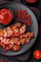 Delicious fresh fried bacon with salt and spices on a dark background photo