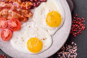 English breakfast with fried eggs, bacon, beans, tomatoes, spices and herbs photo