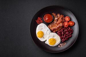 English breakfast with fried eggs, bacon, beans, tomatoes, spices and herbs photo