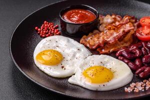 desayuno inglés con huevos fritos, tocino, frijoles, tomates, especias y hierbas foto