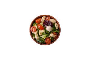 Delicious fresh caprese salad with mozzarella, tomatoes, greens with salt, spices and herbs photo