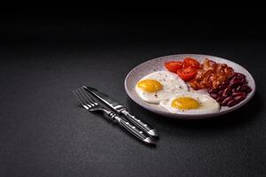 English breakfast with fried eggs, bacon, beans, tomatoes, spices and herbs photo