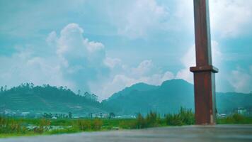 Rural landscape with lush greenery and a concrete pole under a blue sky with fluffy clouds. video