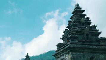 Ancient temple silhouette with intricate carvings against a backdrop of a clear blue sky and distant mountains. video