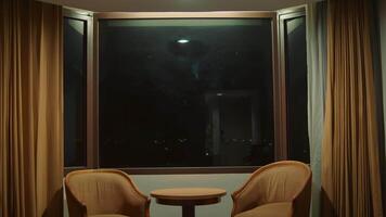 två stolar och en tabell i en vagt belyst rum med stor fönster och gardiner video