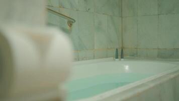 avvicinamento di un' pieno vasca da bagno nel un' bagno con verdastro acqua e piastrelle muri, suggerendo un' rilassante terme ambientazione. video