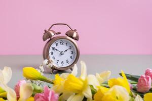 Alarm clock with flowers on pink background. Spring time, daylight savings, spring forward photo