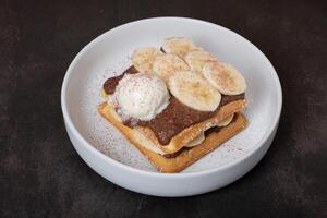 Belgian waffles with banana and chocolate sauce on a dark background photo