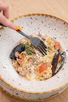 Fork in woman's hand with seafood pasta under delicate cream sauce photo