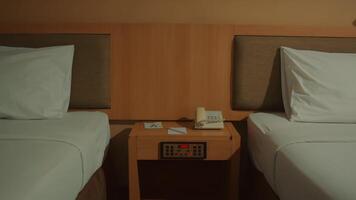 Symmetrical hotel room interior with two single beds and a bedside table with a phone and clock. video