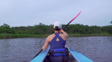A woman is kayaking on a calm river. She is rowing with oars. 4K video
