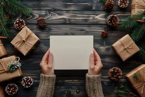 AI generated Person holding blank white sheet of paper for greeting card mockup among collection of Christmas gifts, top view photo