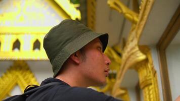 profil de une Jeune homme dans une seau chapeau explorant fleuri d'or architecture, avec une concentrer sur culturel Voyage. video