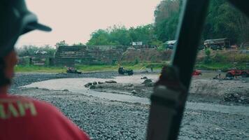 View from a vehicle's passenger seat overlooking a muddy construction site with machinery and scattered debris on a cloudy day. video