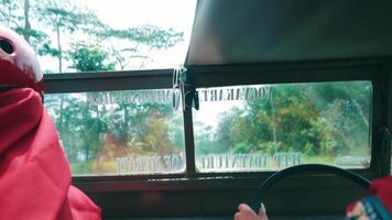 Person in red hoodie looking out a bus window on a rainy day, with water droplets visible on the glass. video