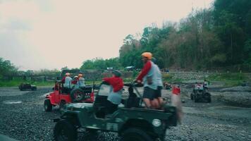 crianças equitação brinquedo atvs em uma cascalho terreno com árvores dentro a fundo e uma branco carro dentro a primeiro plano. video