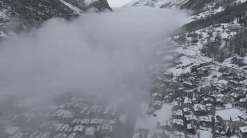 Aerial shot of Zermatt, a tranquil Swiss Alps ski resort, displays chalets and modern facilities under snow. The Matterhorn and snow capped peaks loom behind, creating a serene, majestic winter haven. video