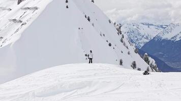 sucesso conceito. uma snowboarder dentro inverno vestuário carrinhos em uma suave declive dentro verboso, Suíça, negligenciar neve limitado montanhas e pinheiros. uma homem em pé em uma pedra penhasco sobre a nuvens. video