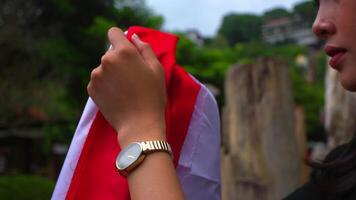 Close-up of a thoughtful woman holding a red fabric, wearing a hat and a watch, with a blurred natural background. video