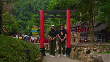 Tourist couple posing under a traditional red torii gate at a historic site with lush greenery in the background. video