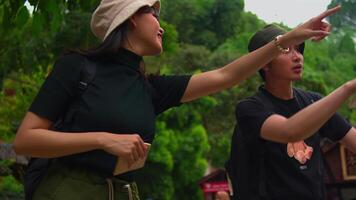 Two young adults exploring, wearing casual clothes and hats, with lush greenery in the background. video