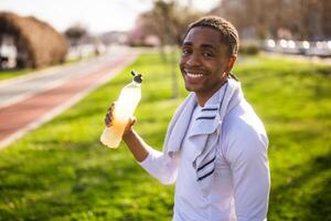 Portrait of young african-american man who is drinking refreshment drink and relaxing after jogging. photo