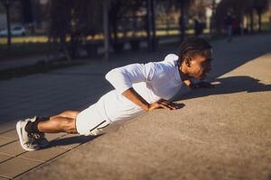 joven afroamericano hombre es hacer ejercicio en el ciudad. él es haciendo Lagartijas. foto