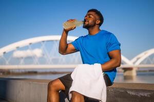 Portrait of young african-american man who is drinking refreshment drink and relaxing after jogging. photo