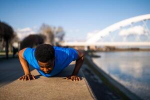 joven afroamericano hombre es hacer ejercicio en el ciudad. él es haciendo Lagartijas. foto