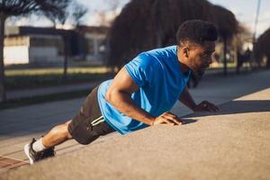 Young african-american man is exercising in the city. He is doing push-ups. photo