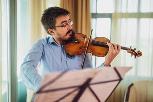 Man playing violin at home. He is practicing for live performance. photo