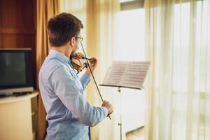 Man playing violin at home. He is cleaning his instrument. photo